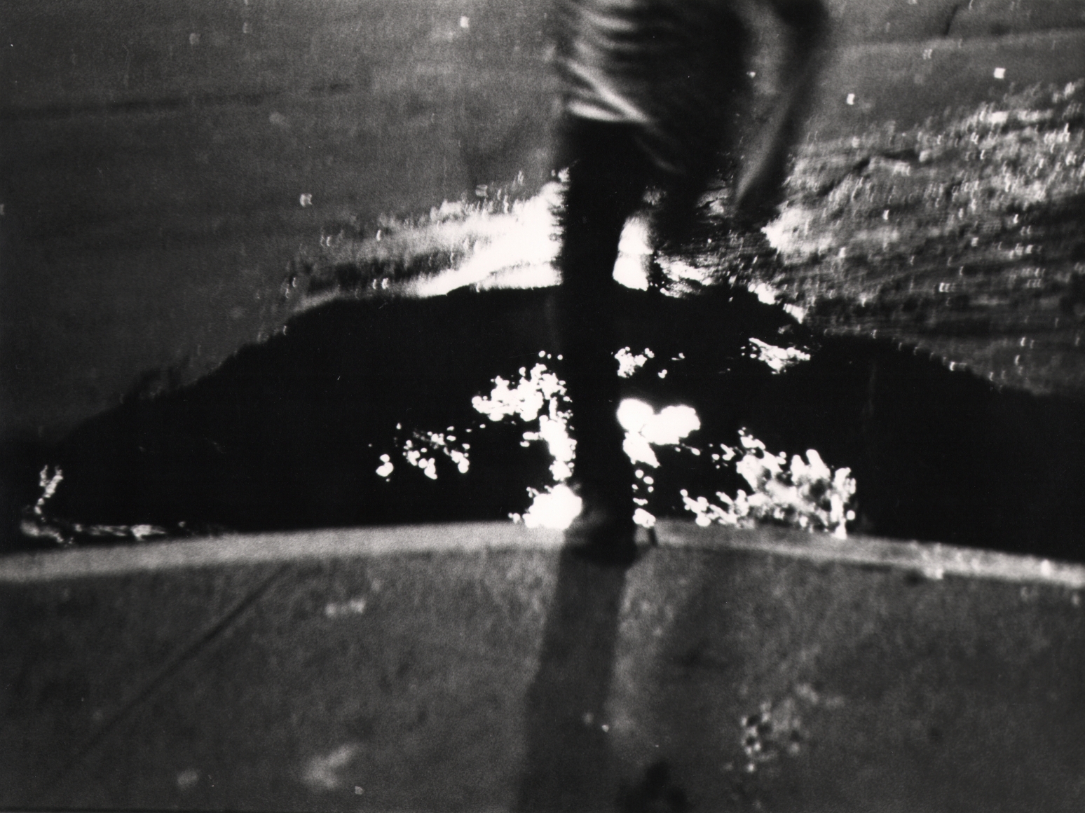 37. Beuford Smith, Untitled, ​c. 1970. Motion-blurred, dark image of the lower body of a boy jumping over a puddle.