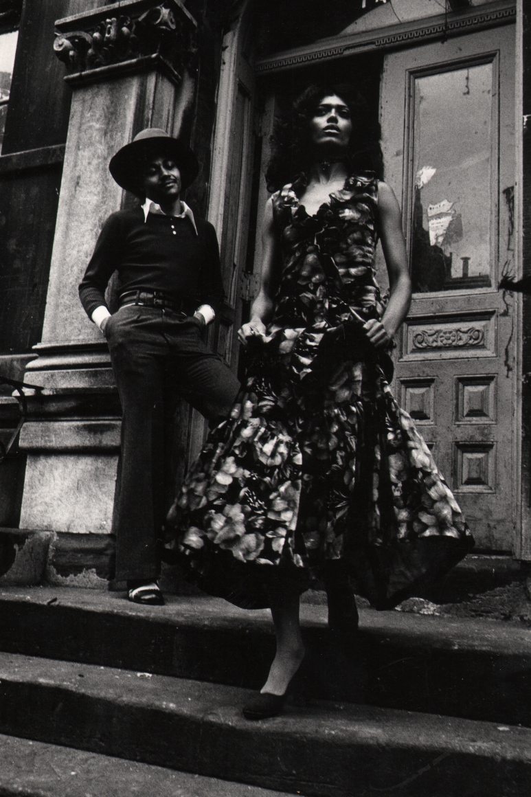 10. Anthony Barboza, Harlem, NY, ​1970s. Sharply-dressed couple in a dress and suit standing at a building entrance.