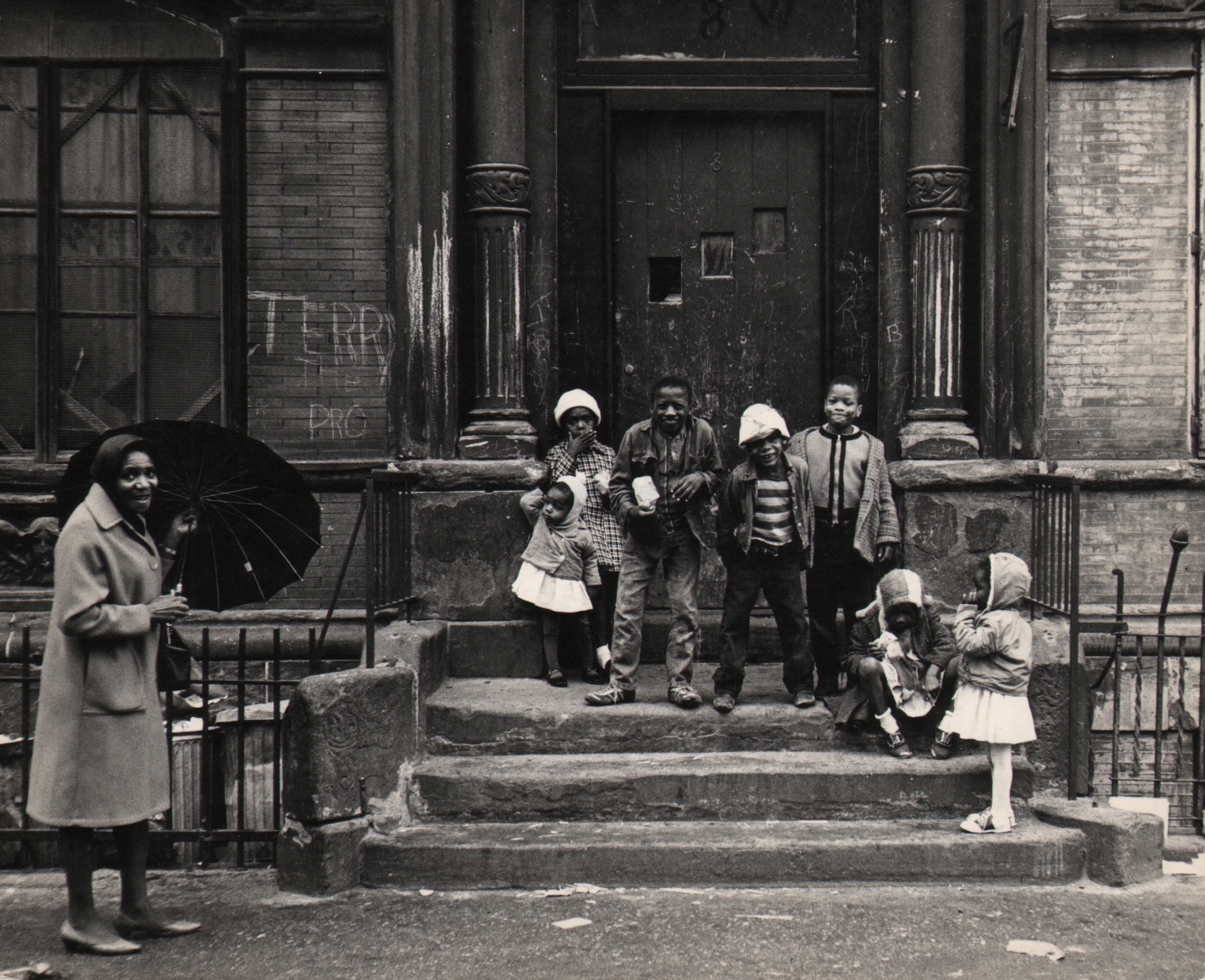 31. Beuford Smith, Harlem Children, Easter Sunday, ​1965. Seven children lined up on a stoop; a smiling woman holding an umbrella stands in the lower left of the frame.