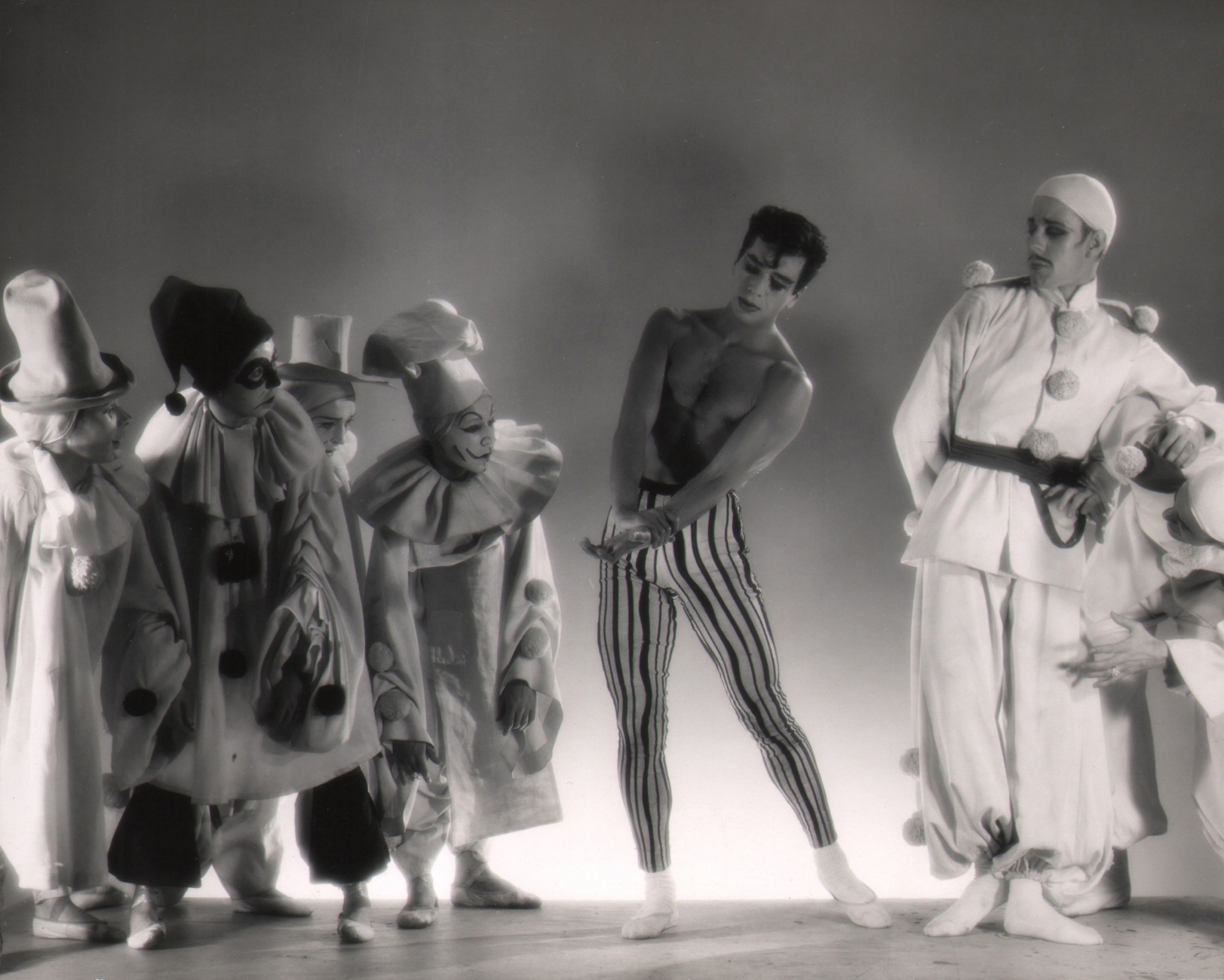 George Platt Lynes, Illumination, Nicholas Magallanes & Brooks Jackson, ​c. 1950. Seven dancers pose in clown costumes. All looking to the central shirtless male figure.