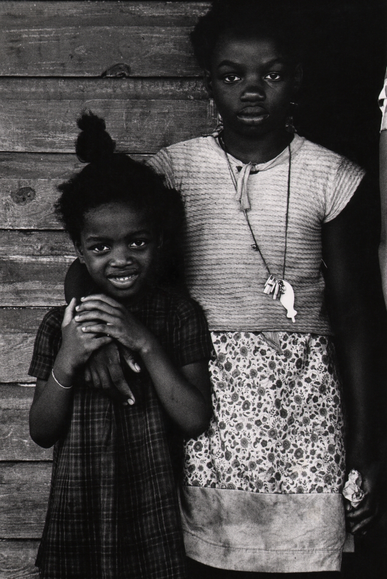 14. Anthony Barboza, Jacksonville, Florida, ​1960s. Two young girls stand side by side, the taller one has her right arm around the other. Both look to the camera; the smaller child is smiling.