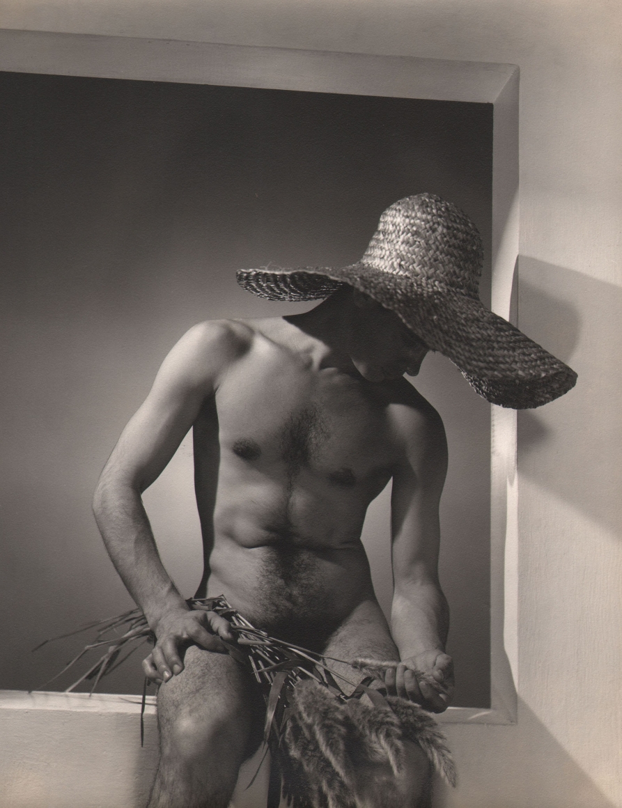 George Platt Lynes, José Martinez, ​c. 1937. Male nude in a straw hat, seated in a window-like opening.