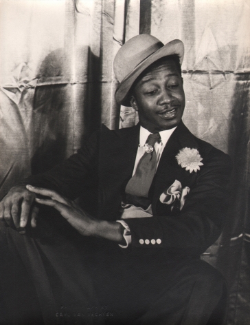 Carl Van Vechten, Avon Long as Sporting Life, Porgy & Bess, ​1942. Subject in a seated pose with legs crossed and hands on knee, looking down and to the right.