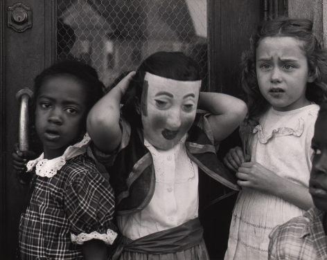 Marvin E. Newman, Chicago, ​1950. Three young girls stand against a door, one wearing a mask.