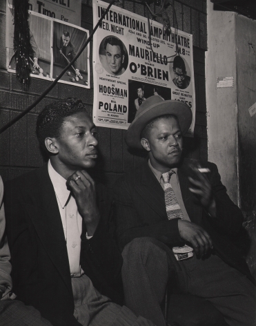 Wayne Miller, Spectators at Pool Hall, Chicago, ​1946–1947. Two men seated against a brick wall with posters on it, both looking to the right. One man holds a cigarette.