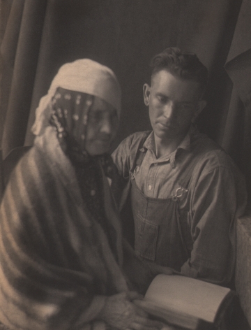 Doris Ulmann, Untitled (Soothsayer), ​1928–1934. Two seated figures, the front-left figure is out of focus and covered in a shawl and headscarves, holding a book. The man on the right looks down at the book.