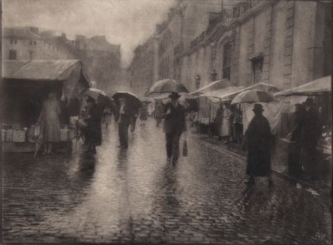 04. Léonard Misonne, Untitled, c. 1930. Figures with umbrellas walk a wet, cobbled market street. Sepia-toned print.