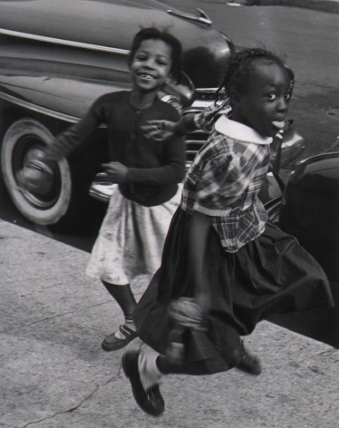 Marvin E. Newman, Chicago, ​1950. Two young girls play on the sidewalk, blurred with motion, smiling at the camera.