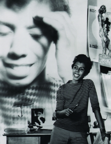 David Attie, Lorraine Hansberry, ​c. 1960. Subject poses leaning against a desk with a close-up photograph of herself superimposed on the wall in the background.