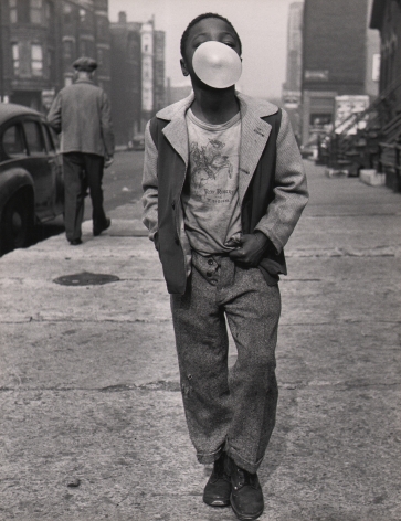 Marvin E. Newman, Chicago, ​1950. A boy walks on the sidewalk toward the camera, hands in pockets, with a chewing gum bubble obscuring most of his face.