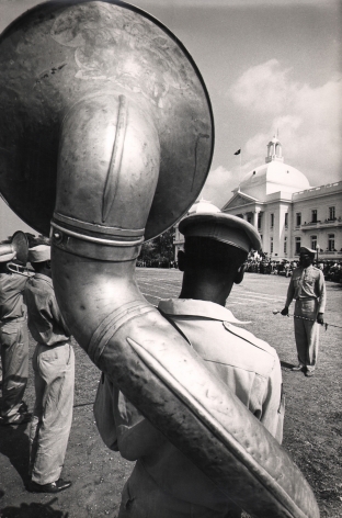 02. Graham Finlayson, Haiti - Presidential band before the Palace, c. 1958–1966. Rear view of a uniformed man with a large wind instrument strapped to his back.