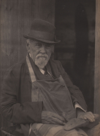 Doris Ulmann, Untitled (Cobbler), ​1928–1934. Seated man in a hat and apron with hands in his lap holding a shoe.