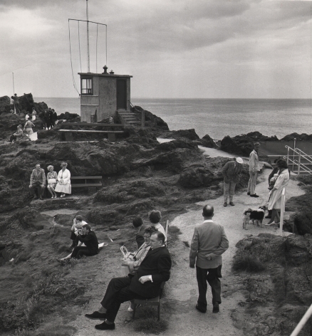 14. C. O'Gorman, A holiday scene at North Berwick with everybody doing something as though compelled by the traditions of seaside behaviourism, 1963. Seaside pathway with scattered figures sitting and standing. A flagpole and small structure stand in the midground left.