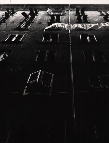 Vittorio Ronconi, Camogli - Le sue case, ​c. 1960. Dark scene looking up at columns of windows of an apartment building. A laundry line hangs across the upper right holding white fabric.