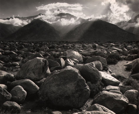 Ansel Adams, Mt. Williamson from Manzanar, Owens Valley, Calif., ​1944. Landscape. Rocks fill the lower half of the frame. Background of mountains and light beams traveling diagonally down and left through clouds.