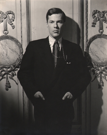 George Platt Lynes, Glenway Wescott, ​n.d. Subject stands in a suit, hands in pockets, against a lavish wall.