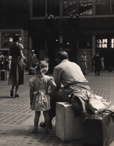 07. Simpson Kalisher, Untitled (Penn Station), ​c. 1949. Rear view of a young girl standing beside a man sitting on a suitcase.