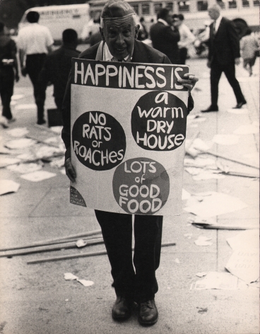 9. LeRoy Henderson, Washington, D.C. Poor People's Campaign, ​1968. Older man stands in the street holding a sign that reads "Happiness is: a warm dry house, no rats, or roaches, lots of good food"