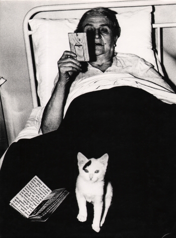 07. Mario Giacomelli, Verrà la morte e avrà i tuoi occhi, 1966–1968. High contrast image. A woman in bed with a book and kitten in her lap, looking at a small frame in her right hand..