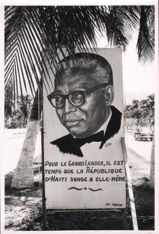 08. Graham Finlayson, Haiti - Crude posters like this one - all of them extolling Duvalier for near-divine virtues, are emblazoned all along the main seafront road in Port au Prince, c. 1958–1966. A poster with a portrait of a man and the words "pour le grand leader, il est temps que la République d'Haiti songe a elle-même"