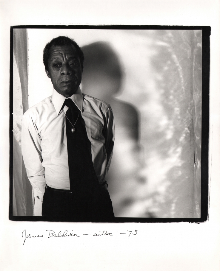 Anthony Barboza, James Baldwin - Author, ​1975. Subject stands to the left of square frame with his shadow cast to the right onto the backdrop.