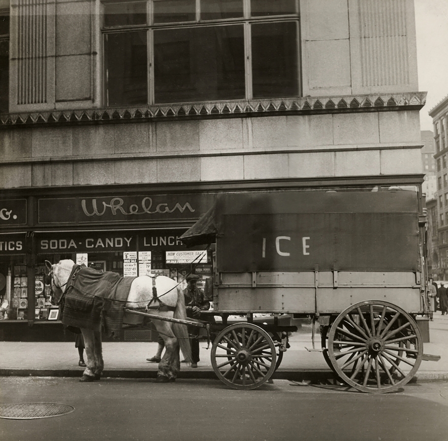 Cecil Beaton, New York, ​c. 1935. A horse-drawn carriage marked "Ice" on the street in front of a building marked "Whelan Soda Candy Lunch"