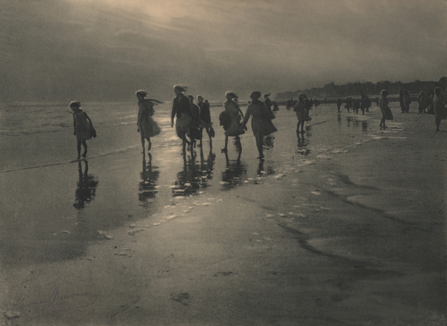 Léonard Misonne, La brise, 1926. A group of girls walk along the beach with bare feet in the water. Gray/green-toned print.