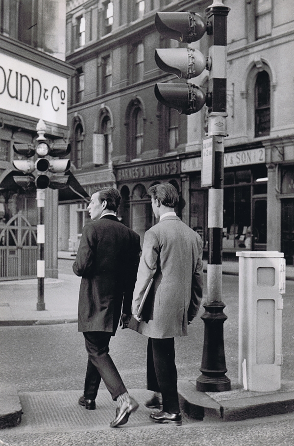 Henri Cartier-Bresson, Teddy Boys on Oxford Street, ​c. 1955. Two men, back to the camera, walk across a city street, passing a traffic light on the right.